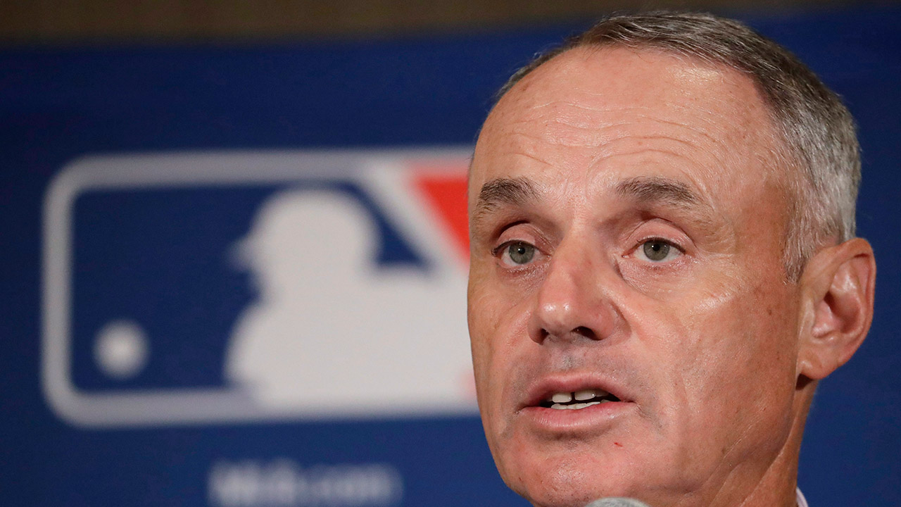 Major-League-Baseball-Commissioner-Rob-Manfred-answers-questions-at-a-news-conference-in-Phoenix.-The-Los-Angeles-Dodgers-and-New-York-Yankees-are-cutting-payroll-and-their-luxury-tax-bills,-just-as-Bryce-Harper,-Manny-Machado-and-perhaps-Clayton-Kershaw-near-the-free-agent-market-after-the-2018-season.-"What-the-market-produces-is-what-the-market's-going-to-produce,"-Manfred-said.-(Morry-Gash/AP)