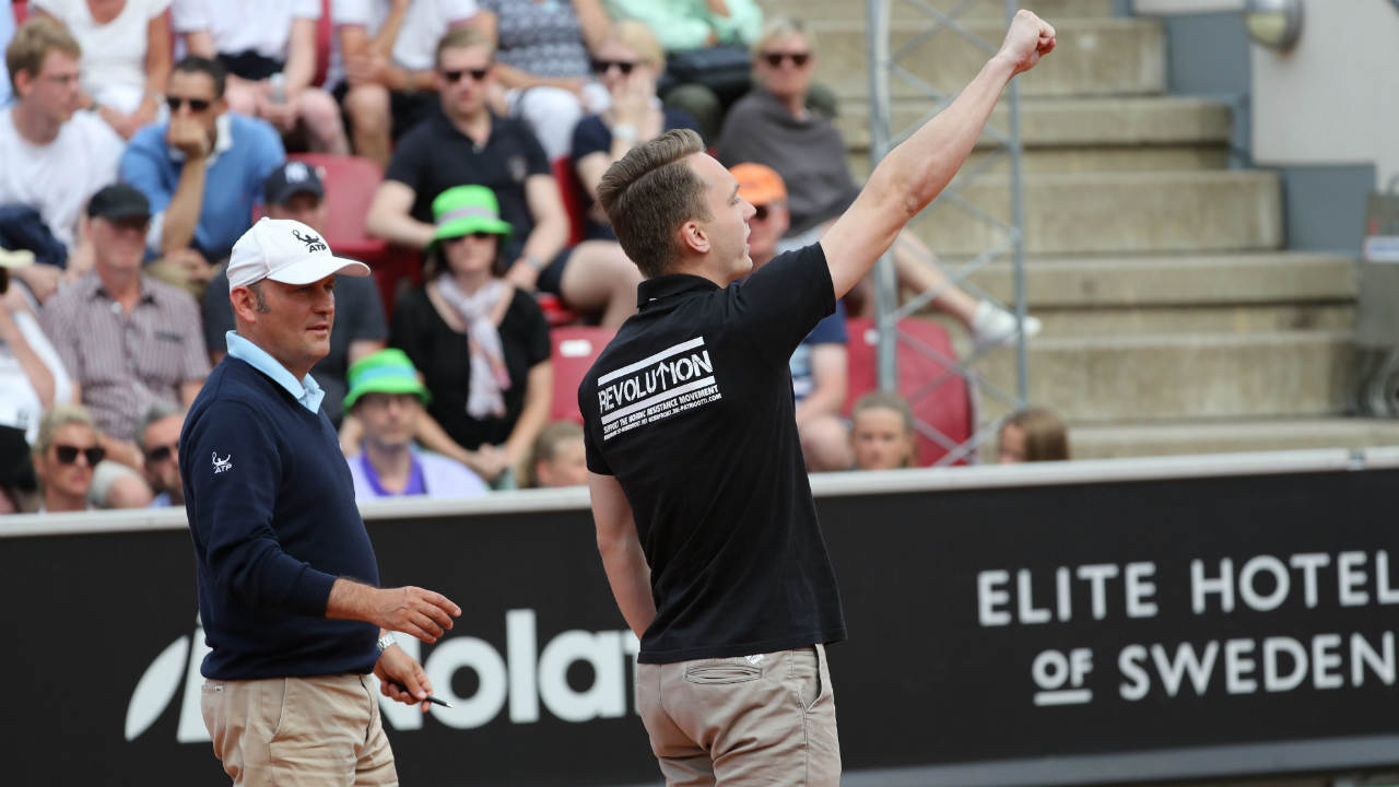 A-man-in-a-black-T-shirt-supporting-Revolution,-a-Nordic-resistance-movement-gestures-as-he-is-escorted-off-the-court-by-security,-during-the-ATP-tennis-tournament-Swedish-Open-semifinal-match-between-Fernando-Verdasco-and-David-Ferrer,-in-Bastad,-Sweden,-Saturday-July-22,-2017.-(Adam-Ihse/TT-via-AP)