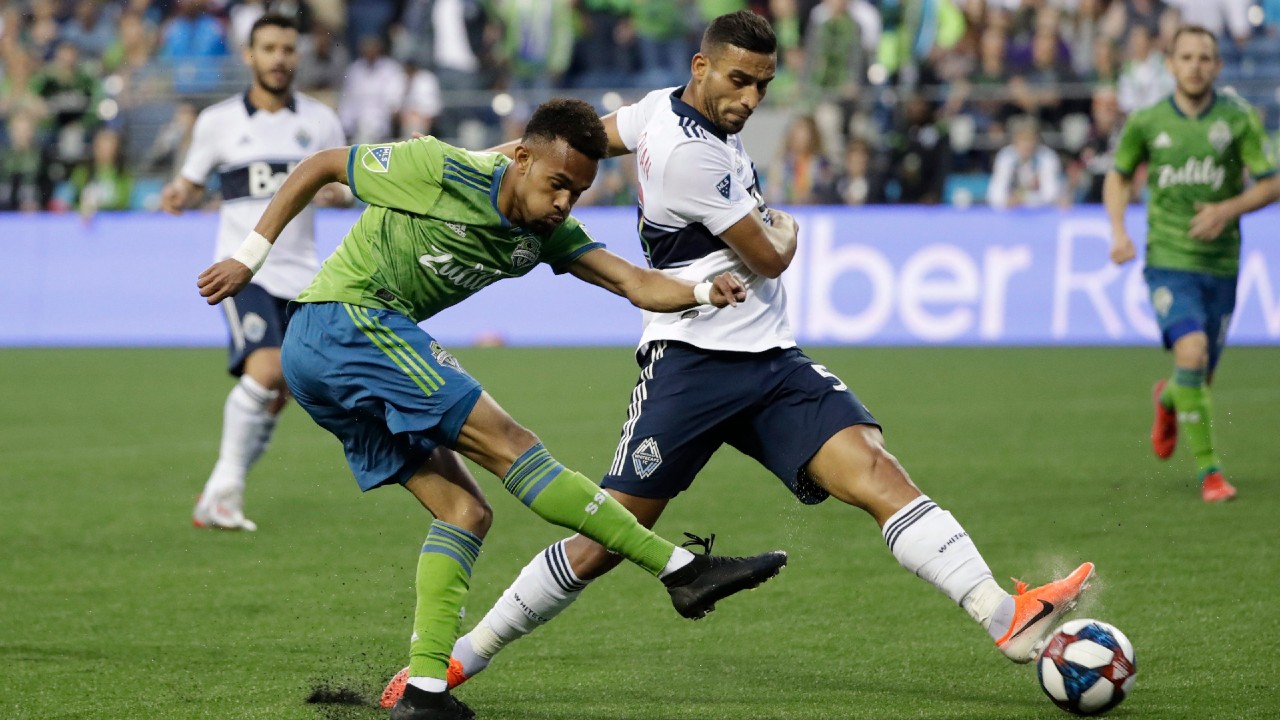 Seattle Sounders' Handwalla Bwana, left, takes a shot past Vancouver Whitecaps' Ali Adnan. (Elaine Thompson/AP)