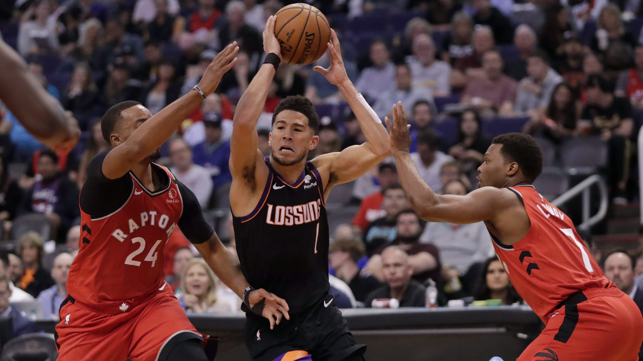 Phoenix Suns guard Devin Booker (1) drives between Toronto Raptors guard Norman Powell (24) and guard Kyle Lowry (7) during the second half of an NBA basketball game Tuesday, March 3, 2020, in Phoenix. The Raptors won 123-114. (Matt York/AP)