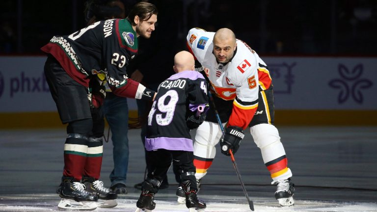 Arizona Coyotes' Oliver Ekman-Larsson (23) drops the puck in front of Leighton Accardo, middle, who is battling cancer, and Calgary Flames' Mark Giordano (5) during an NHL Fights Cancer puck drop ceremony prior to an NHL hockey game in Glendale, Ariz., in this Saturday, Nov. 16, 2019, file photo. Accardo's will to attack anything in her path, even terminal cancer, lifted an entire organization. The Arizona Coyotes will carry her spirit on by making her the first non-player, general manager or broadcaster to be inducted into an NHL team's ring of honor. (AP Photo/Ross D. Franklin, File)