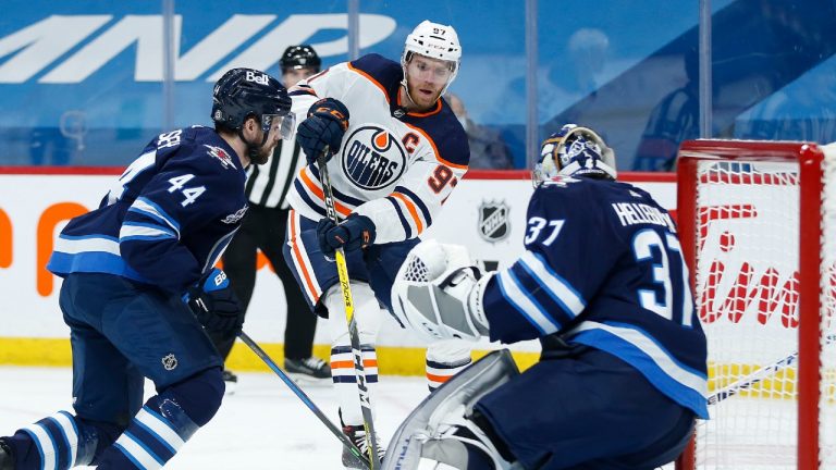 Winnipeg Jets goaltender Connor Hellebuyck (37) saves the shot from Edmonton Oilers' Connor McDavid (97) as Jets' Josh Morrissey (44) defends during first period NHL action in Winnipeg on Wednesday, April 28, 2021. (John Woods/CP)