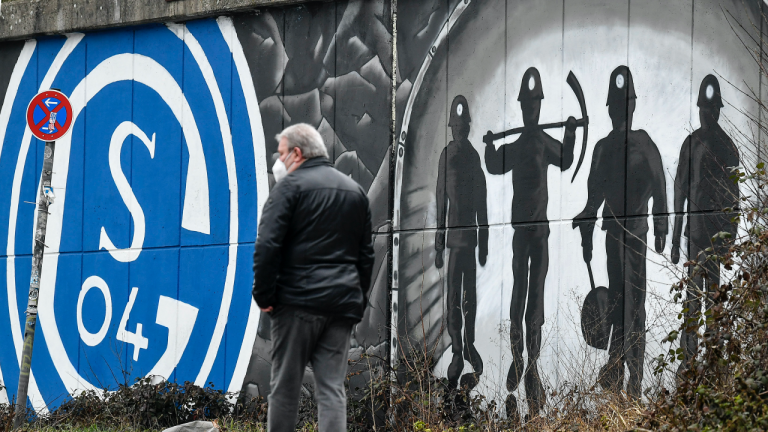 A man passes graffiti on wall with the logo of Bundesliga soccer club FC Schalke 04 and coal miners in the light at the end of the tunnel in Gelsenkirchen, Germany, Monday, March 1, 2021. (Martin Meissner / AP)