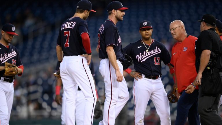 Washington Nationals starting pitcher Max Scherzer, centre, stands on the mound as a trainer comes to check on him during the first inning of the team's baseball game against the San Francisco Giants, Friday, June 11, 2021, in Washington. Scherzer left the game with an injury. Nationals shortstop Trea Turner is at centre left. (Nick Wass/AP)