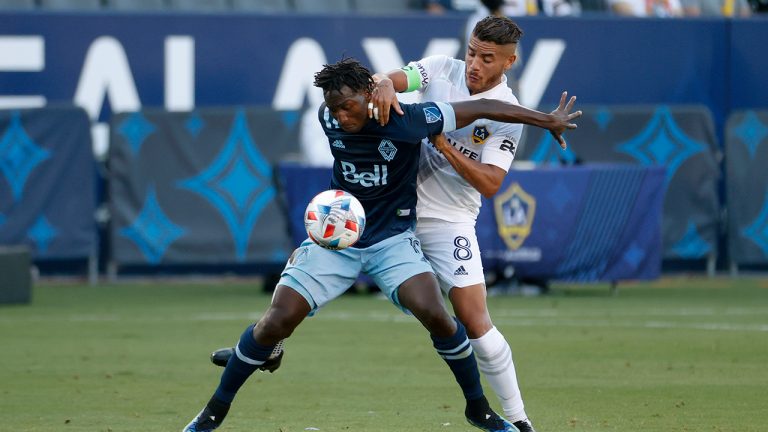Vancouver Whitecaps midfielder Janio Bikel, left, and LA Galaxy midfielder Jonathan dos Santos (8) vie for the ball in the second half of an MLS soccer match in Carson, Calif., Sunday, Aug. 8, 2021. The game ended in a 1-1 draw. (Ringo H.W. Chiu/AP)