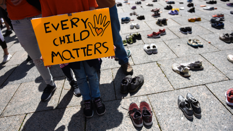 People stand on Parliament Hill alongside a memorial for children who died at Indian Residential Schools, during a rally to demand an independent investigation into Canada's crimes against Indigenous Peoples, in Ottawa on Saturday, July 31, 2021. (Justin Tang / CP)