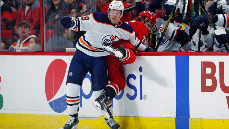Edmonton Oilers' Tyler Benson (49) checks Carolina Hurricanes' Brock McGinn (23) into the bench during the first period of an NHL hockey game in Raleigh, N.C., Sunday, Feb. 16, 2020. (Karl B DeBlaker / AP)