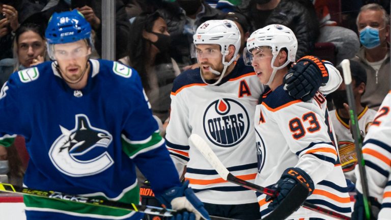 Edmonton Oilers' Leon Draisaitl (centre) celebrates with teammate Ryan Nugent-Hopkins (right) after scoring a goal as Vancouver Canucks' Juho Lammikko skates past during second period NHL hockey action in Vancouver, B.C., Saturday, Oct. 30, 2021. (Rich Lam/CP)