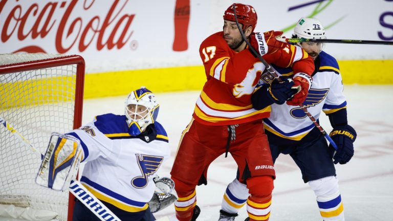 St. Louis Blues' Justin Faulk, right, checks Calgary Flames' Milan Lucic as goalie Ville Husso follows the play during third period NHL hockey action in Calgary, Alta., Monday, Jan. 24, 2022. (Jeff McIntosh/CP)