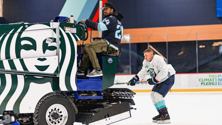 In this photo provided by the Seattle Kraken NHL hockey team, former Seattle Seahawks NFL football running back Marshawn Lynch, left, drives an ice surfacing machine as Grammy winning musician Macklemore skates behind it on March 16, 2022, in Seattle. The expansion Seattle Kraken announced Monday, April 18, 2022 that Lynch and Macklemore had become part of the minority investor group for the franchise. (Caean Couto/Seattle Kraken via AP)