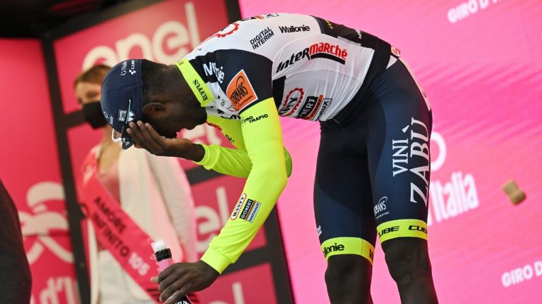Eritrea's Biniam Girmay touches his eye after spraying sparkling wine on the podium to celebrate winning the 10th stage of the Giro D'Italia cycling race from Pescara to Jesi, Italy, Tuesday, May 17, 2022. Girmay was then taken to a local hospital after getting injured when he popped a champagne cork into his eye during the podium celebration. (Massimo Paolone/LaPresse via AP)