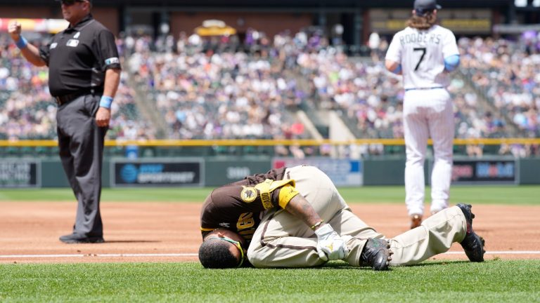 San Diego Padres' Manny Machado grips his left ankle after falling over first base while trying to beat out an infield hit to Colorado Rockies starting pitcher Antonio Senzatela in the first inning of a baseball game, Sunday, June 19, 2022, in Denver. Machado was helped off the field and was called out on the play. (David Zalubowski/AP)