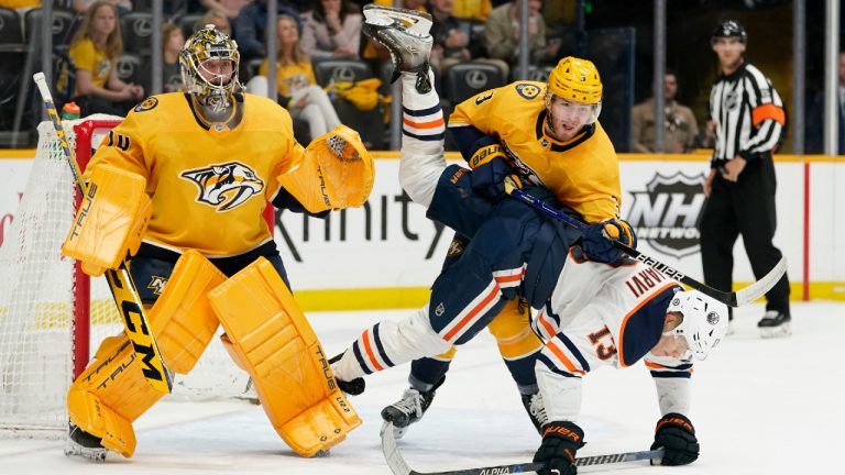 Edmonton Oilers' Jesse Puljujarvi (13) is checked by Nashville Predators' Jeremy Lauzon (3) as Predators goaltender Juuse Saros (74) watches the play in the first period of an NHL hockey game Thursday, April 14, 2022, in Nashville, Tenn. (Mark Humphrey/AP)