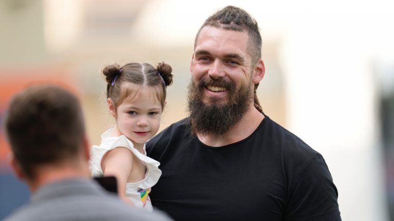 Former Denver Broncos defensive lineman Derek Wolfe, right, holds a child as he is greeted by media members while attending the NFL football team's training camp Friday, July 29, 2022, in Centennial, Colo. Wolfe signed a one-day contract with the Broncos to retire as a Denver player on Friday. (David Zalubowski/AP)
