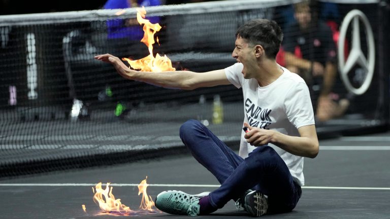 A man sets fire on his hand during protest at a match Team World's Diego Schwartzman against Team Europe's Stefanos Tsitsipas on day one of the Laver Cup tennis tournament at the O2 in London, Friday, Sept. 23, 2022. (AP Photo/Kin Cheung)
