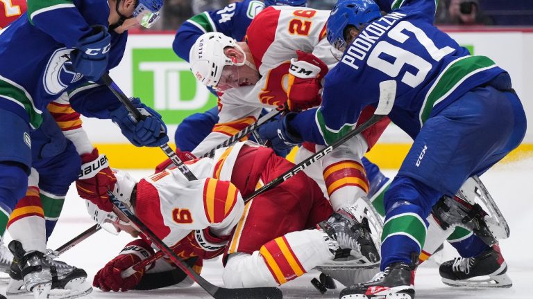 Calgary Flames' Michael Stone (26) and Juuso Valimaki (6), of Finland, vie for the puck against Vancouver Canucks' Vasily Podkolzin (92), of Russia, during the second period of a pre-season NHL hockey game in Vancouver, B.C., Sunday, Sept. 25, 2022. (Darryl Dyck/CP)