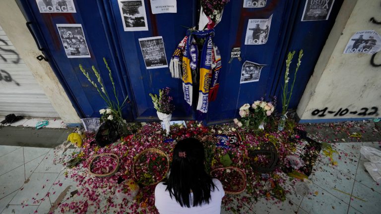 A woman takes a moment for the victims of Saturday's soccer match stampede in front of gate 13 the Kanjuruhan Stadium in Malang, Indonesia, Tuesday, Oct. 4, 2022. Indonesian police said Tuesday that the gates at the soccer stadium where police fired tear gas and set off a deadly crush were too small and could only accommodate two at a time when hundreds were trying to escape.(Achmad Ibrahim/AP)