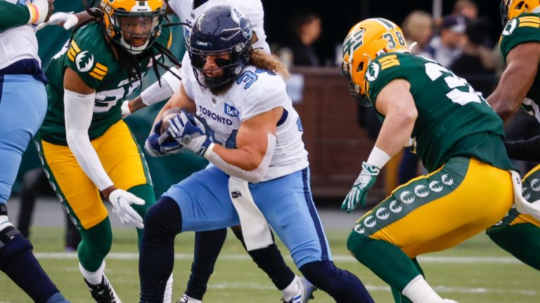 Toronto Argonauts' A.J. Ouellette, centre, runs the ball as Edmonton Elks' Adam Konar, right, lines up the tackle during first half CFL football action in Edmonton, Saturday, Oct. 15, 2022. (Jeff McIntosh/CP)