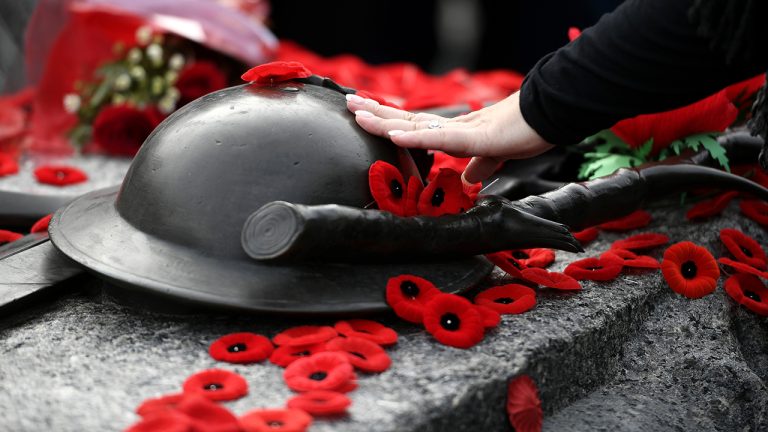 A person touches the helmet on the Tomb of the Unknown Soldier after laying a poppy, at the National War Memorial after the National Remembrance Day Ceremony in Ottawa, on Friday, Nov. 11, 2022. (Justin Tang/CP)