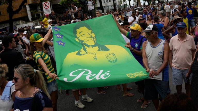 People hold a banner of the late Brazilian soccer great Pele along the route of his funeral procession from Vila Belmiro stadium to the cemetery in Santos, Brazil, Tuesday, Jan. 3, 2023. (Matias Delacroix/AP)