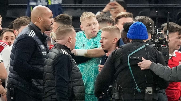 Arsenal goalkeeper Aaron Ramsdale, in green, is ushered away after an incident at the end of the English Premier League soccer match between Tottenham Hotspur and Arsenal at the Tottenham Hotspur Stadium in London, England, Sunday, Jan. 15, 2023. The incident happened when a spectator climbed onto an advertising board and appeared to kick Ramsdale after the team's 2-0 win over Tottenham in the Premier League. (Frank Augstein/AP Photo)