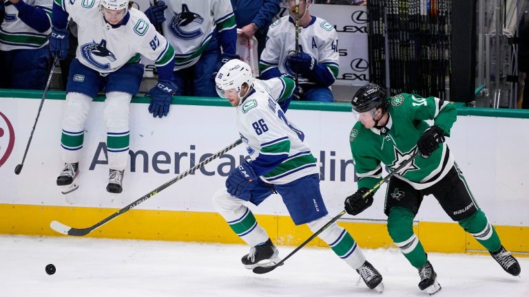 Vancouver Canucks defenseman Christian Wolanin (86) moves to control the puck in front of Dallas Stars' Ty Dellandrea (10) as Canucks' Vasily Podkolzin (92) sits on the bench wall in the third period of an NHL hockey game, Monday, Feb. 27, 2023, in Dallas. (Tony Gutierrez/AP Photo)