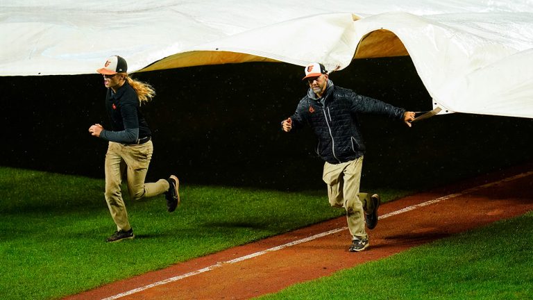 Grounds crew members place a tarp over the infield at Oriole Park at Camden Yards during a rain delay in the eighth inning of a baseball game between the Baltimore Orioles and the Toronto Blue Jays, Monday, Oct. 3, 2022, in Baltimore. (Julio Cortez/AP)