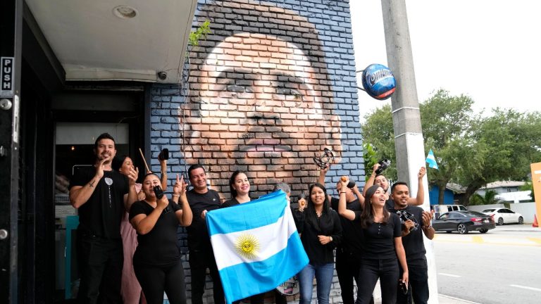 Staff at the Fiorito restaurant hold an Argentinian flag as they pose for a photograph taken by a colleague in front of a mural of Lionel Messi, Wednesday, June 7, 2023, in Miami. The Argentine soccer star announced Wednesday he is joining the Inter Miami Major League Soccer team. (Lynne Sladky/AP)