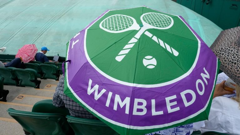 Spectators sit under an umbrella on a covered court after rain delayed the start of play on day three of the Wimbledon tennis championships in London, Wednesday, July 5, 2023. (AP Photo/Kirsty Wigglesworth)