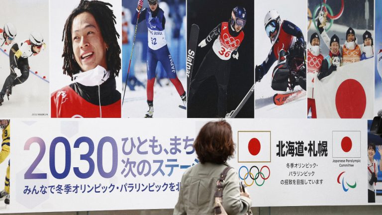 A pedestrian passes by a poster of Sapporo's bid for 2030 Winter Olympics in Sapporo, northern Japan on Oct. 6, 2023. Sapporo and Japanese Olympic Committee on Wednesday officially announced a decision to withdraw the northern Japanese city as a candidate to host the 2030 Winter Olympics, its bid soiled by massive corruption and bid-rigging tied to the one-year delayed 2020 Tokyo Games. (Kyodo News via AP)