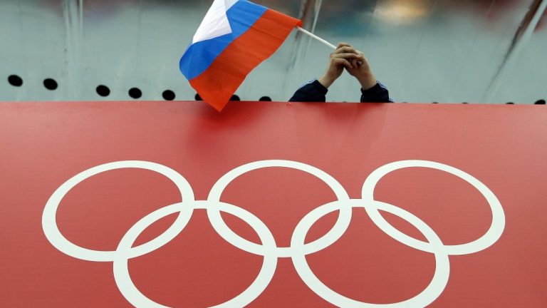 A Russian flag is held above the Olympic Rings at Adler Arena Skating Center during the Winter Olympics in Sochi, Russia on Feb. 18, 2014. (AP Photo/David J. Phillip)