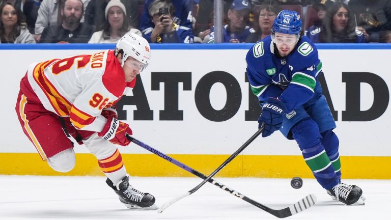 Calgary Flames' Andrei Kuzmenko (96) and Vancouver Canucks' Quinn Hughes (43) vie for the puck during the first period of an NHL hockey game in Vancouver, on Tuesday, April 16, 2024. (Darryl Dyck/THE CANADIAN PRESS)