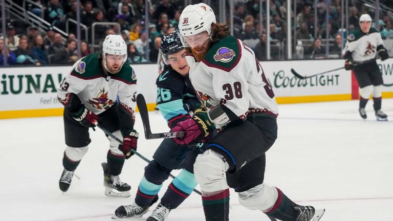 Seattle Kraken center Ryan Winterton, center, reaches through the legs of Arizona Coyotes center Liam O'Brien (38) for the puck as left wing Michael Carcone, left, looks on during the second period of an NHL hockey game Tuesday, April 9, 2024, in Seattle. (Lindsey Wasson/AP)