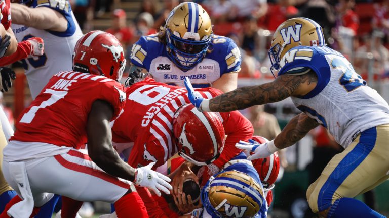 Winnipeg Blue Bombers' quarterback Zach Collaros (8) is sacked by Calgary Stampeders' James Vaughters (9) and Micah Awe (7) during first half CFL football action in Calgary, Alta., Saturday, June 29, 2024. (Jeff McIntosh/CP)