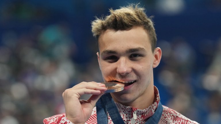 Ilya Kharun, of Canada, bites down on his bronze medal after competing in the men's 200-metre butterfly final at the 2024 Summer Olympics in Nanterre, France on Wednesday, July 31, 2024. (Nathan Denette/THE CANADIAN PRESS)