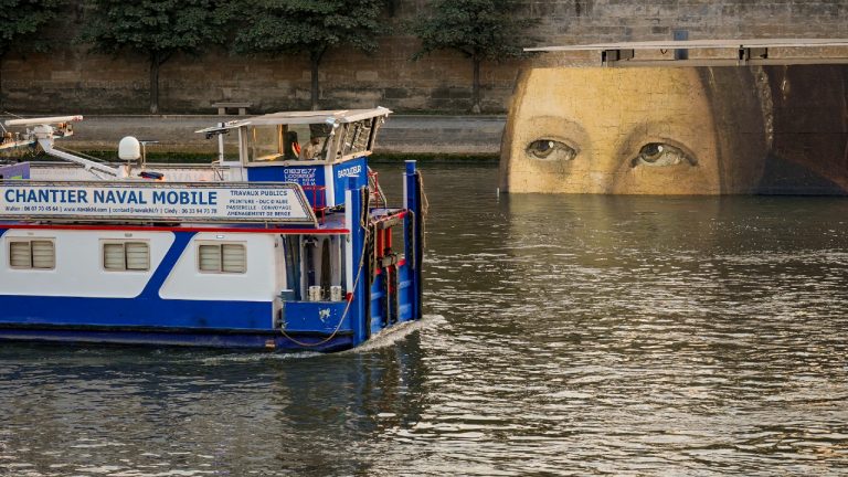 A ship sails past reproductions of artworks decorating the banks of the River Seineat the 2024 Summer Olympics, Tuesday, July 30, 2024, in Paris, France. The men's Olympic triathlon has been postponed over concerns about water quality in Paris' Seine River, where the swimming portion of the race was supposed to take place. (Dar Yasin/AP)