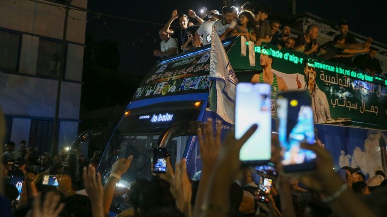 Olympic gold medalist in the the women's 66 kg boxing Algeria's Imane Khelif, top center, waves from the top of a double decker bus while surrounded by fans as she returns home from the 2024 Paris Olympic Games in Tiaret, Algeria, Friday, Aug. 16, 2024. (Anis Belghoul/AP)