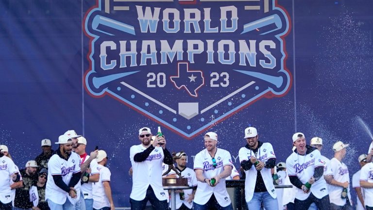 The Texas Rangers, on stage, spray champagne on fans during a World Series championship celebration, Nov. 3, 2023. (AP Photo/Julio Cortez)