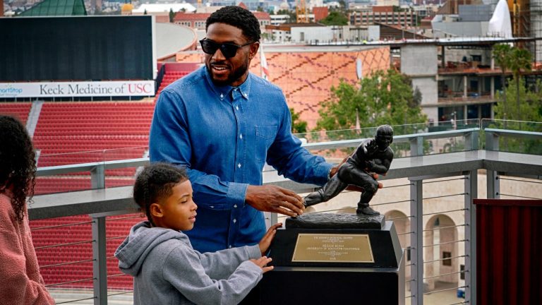 Former USC football player Reggie Bush, with the help from his son, places his returned Heisman Trophy on a pedestal prior a news conference at the Los Angeles Memorial Coliseum, Thursday, April, 25, 2024, in Los Angeles. (Richard Vogel/AP)