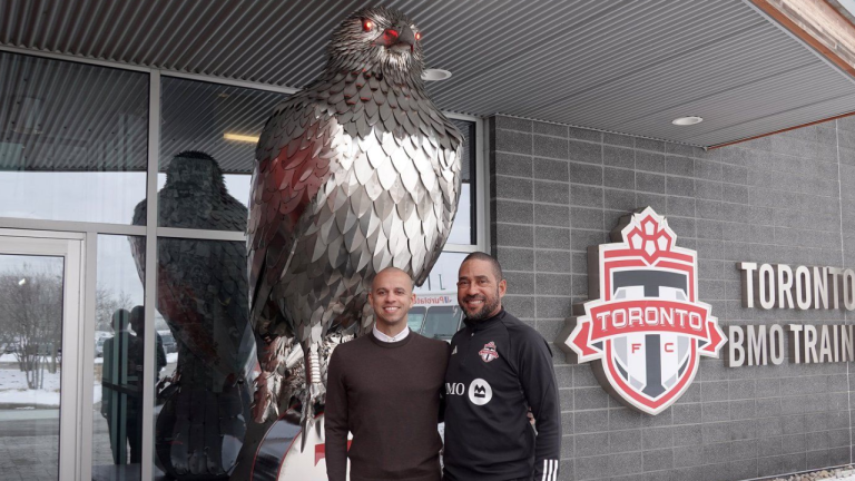 Toronto FC GM Jason Hernandez, left, and newly named head coach Robin Fraser pose in front of a statue of a giant hawk, the club mascot, outside the MLS club’s training centre, in Toronto. (CP/Neil Davidson)