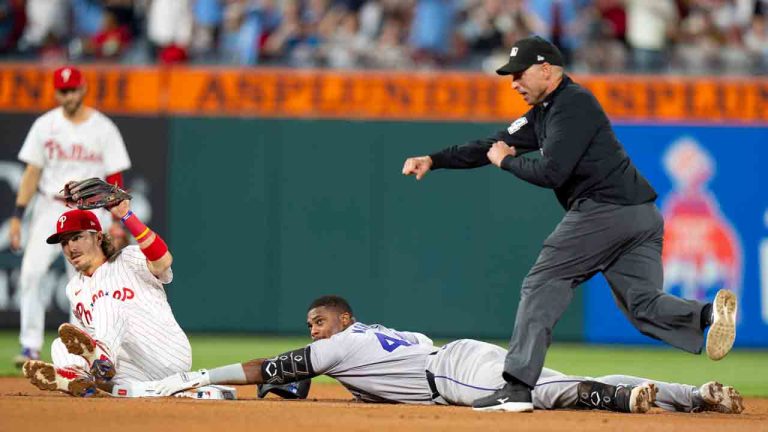 Philadelphia Phillies second baseman Bryson Stott, left, holds up the ball in his glove after putting out Colorado Rockies' Elehuris Montero, center, who tried to stretch a single into a double, as umpire Paul Clemons, right, makes the call during the seventh inning of a baseball game Tuesday, April 16, 2024, in Philadelphia. The Phillies won 5-0. (Chris Szagola/AP)