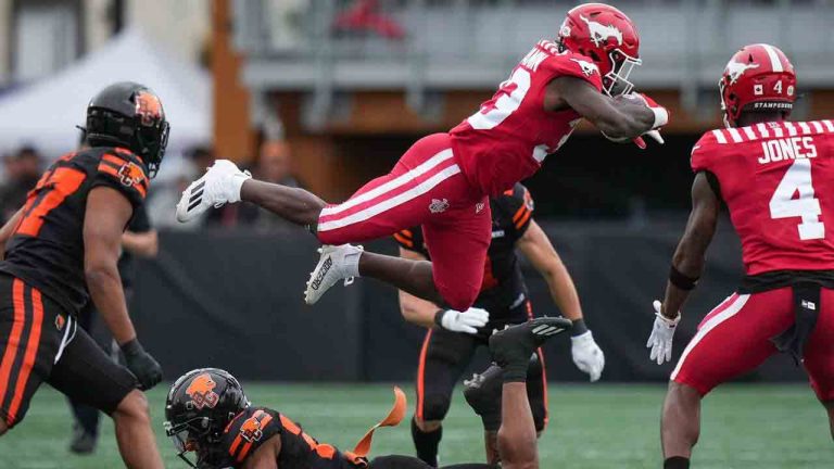 Calgary Stampeders' Eno Benjamin, back top, leaps over B.C. Lions' Jordan Perryman to avoid a tackle during the first half of a preseason CFL football game, in Langford, B.C., on Monday, May 19, 2025. (Darryl Dyck/CP)