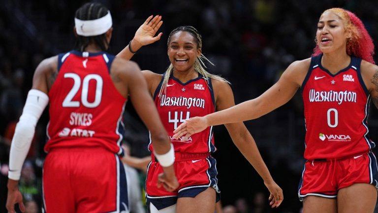 Washington Mystics guard Brittney Sykes (20) is greeted by forward Kiki Iriafen (44) and forward Shakira Austin (0) as they celebrate a lead over the Seattle Storm late during the second half of a WNBA basketball game Sunday, July 13, 2025, in Seattle. (AP Photo/Lindsey Wasson)