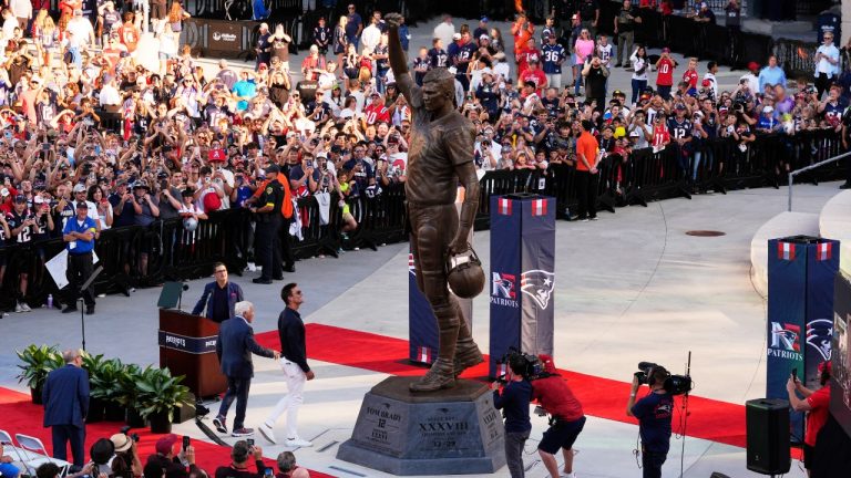 Former New England Patriots quarterback Tom Brady, center left, looks at a bronze statue of himself after it was unveiled in Patriot Place Plaza before an NFL preseason football game between the Washington Commanders and the New England Patriots Friday, Aug. 8, 2025, in Foxborough, Mass. (Charles Krupa/AP)