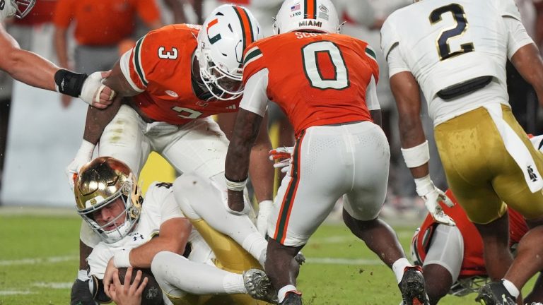 Notre Dame quarterback CJ Carr, left, falls to the field as Miami defensive lineman Akheem Mesidor (3) and defensive back Keionte Scott (0) defend during the first half of an NCAA college football game, Sunday, Aug. 31, 2025, in Miami Gardens, Fla. (Lynne Sladky/AP Photo)