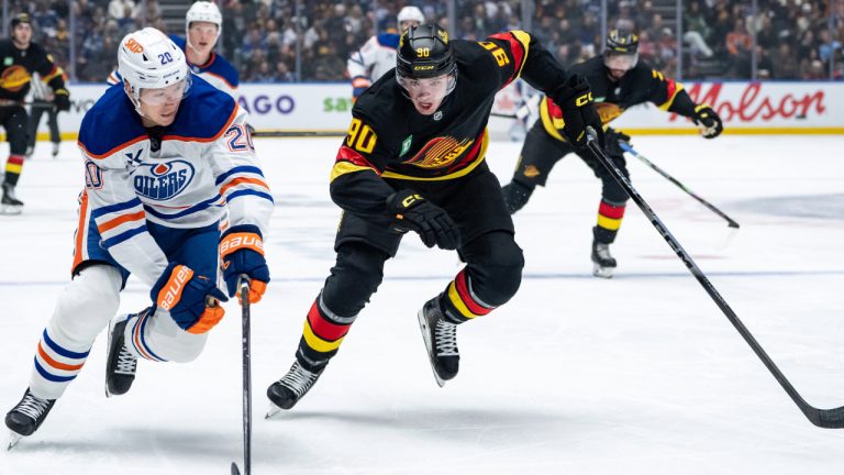Edmonton Oilers' Curtis Lazar and Vancouver Canucks' Victor Mancini vie for the puck during first period NHL action in Vancouver, B.C., Sunday, Oct. 26, 2025. (Ethan Cairns/CP)