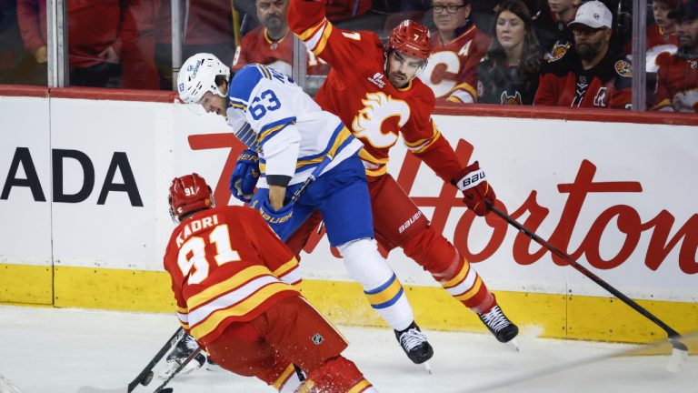 St. Louis Blues' Jake Neighbours, centre, is checked by Calgary Flames' Nazem Kadri, left, and Kevin Bahl during first period NHL hockey action in Calgary, Alta., Saturday, Oct. 11, 2025. (Jeff McIntosh/CP)