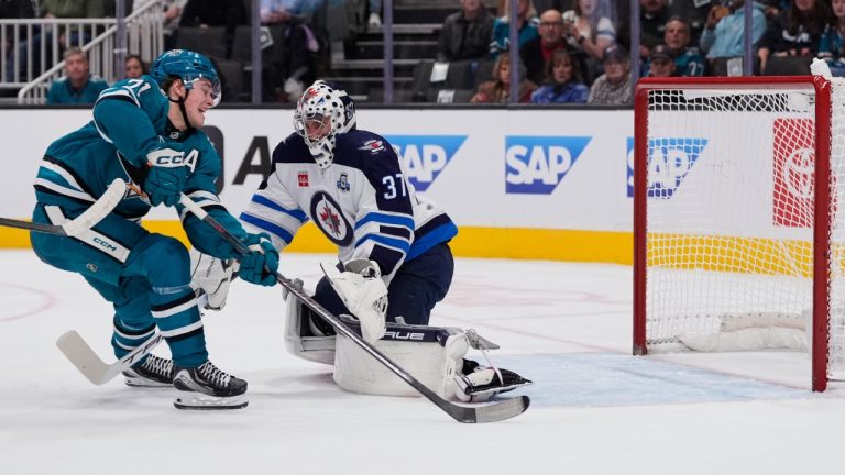 San Jose Sharks center Macklin Celebrini, left, shoots in front of Winnipeg Jets goaltender Connor Hellebuyck (37) during the first period of an NHL hockey game, Friday, Nov. 7, 2025, in San Jose, Calif. (AP Photo/Godofredo A. Vásquez)
