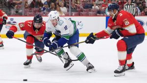 Vancouver Canucks left wing Drew O'Connor (18) pushes through Florida Panthers defenceman Niko Mikkola (77) and Seth Jones (3) during the first period of an NHL hockey game, Monday, Nov. 17, 2025, in Sunrise, Fla. (Rebecca Blackwell/AP)