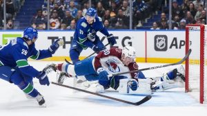 Colorado Avalanche's Ross Colton (20) trips over Vancouver Canucks goalie Kevin Lankinen, back right, after being slashed by Tyler Myers (57) as Marcus Pettersson (29) watches during the first period of an NHL hockey game in Vancouver, B.C., Sunday, Nov. 9, 2025. (Darryl Dyck/CP)